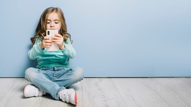 Menina sentada no chão mexendo num smartphone.