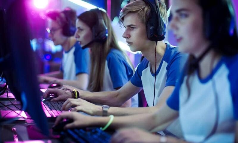 Na fotografia há dois garotos e duas garotas, todos brancos. Eles estão vestindo uma camiseta branca e azul como uniforme. Eles estão em frente a computadores, por onde estão jogando jogos eletrônicos.